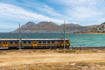 Glencairn, Cape Town, South Africa. December 2019. Coastal passenger train passing the resort of Glencairn on the coast to Simons Town where it terminates.