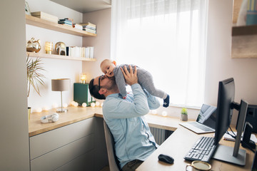 Young father working from home and babysitting his baby boy.