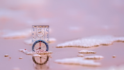 Compass on a beach with creamy surf and reflections in wet sand against an ocean background