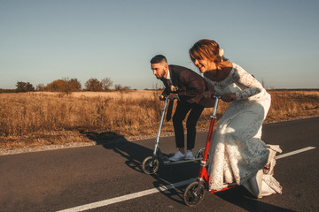 Smiling wedding couple riding a on scooters along the road outside the city at sunset. Place for...