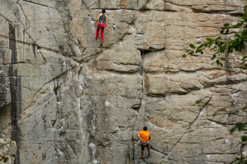 A young woman with a rope engaged in the sports of rock climbing on the rock.