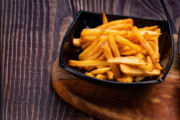 a potatoes fries in black dish  wooden Board.