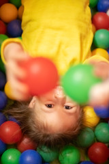 Fototapeta na wymiar Little girl in a ball pit smiling at the camera, raising hands, having fun at the children play center