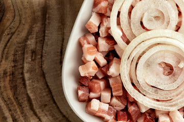Italian pancetta, bacon cubes, diced ham, cutted pork, sliced onion in square white plate on wooden textured surface. Cooking ingredient for pasta carbonara italian dish. Top view, close up.