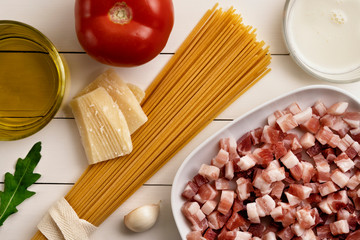 Cooking ingredients on white wooden rustic background. Pasta, uncoocked spaghetti, egg, parmesan, pancetta bacon, ham, cream, garlic, olive oil, tomato. Top view, flat lay
