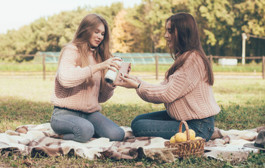  Girlfriends drink tea outdoors in identical sweaters sitting on a plaid
