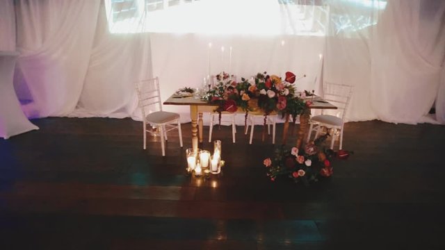 Top view of wedding table for groom and bride on the white background with chiavari chairs and floral composition made of red flowers, place in the restaurant for romantic date with burning candles