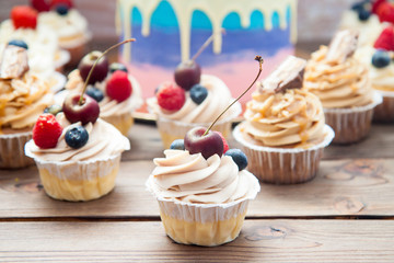 Cheesecake cupcake with cream cheese frosting and fresh cherry on top, wooden background.
