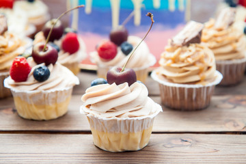 Cheesecake cupcake with cream cheese frosting and fresh cherry on top, wooden background.