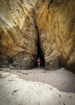 Mujer con biquini rojo saliendo de una cavidad entre las rocas de una playa cerca de Sines en portugal