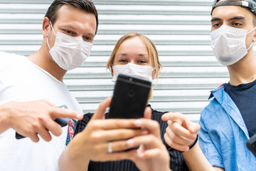 Three young people of different ethnicities with protective masks on their faces using a mobile