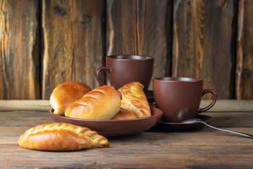 plate with fresh hot mini pies and coffee cups on wooden table, close view