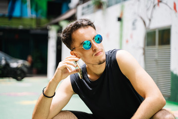 Young man with sunglasses crouching in the middle of the street talking to a mobile phone