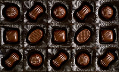Assorted chocolates lying in a box. Background for products from chocolate and sweets. Dark chocolate.