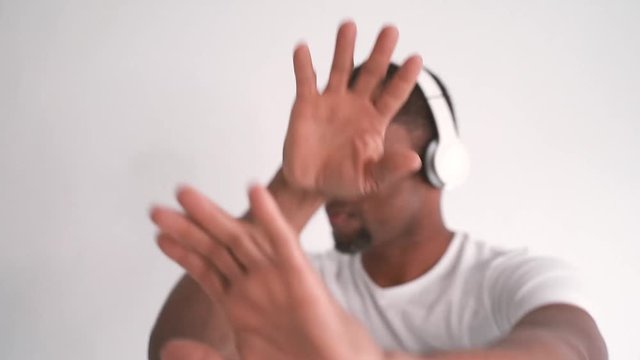 Isolated african american young man dancing with rhythm at home. Attractive cuban man moving his body dancing at white background with headphones. Indoors music and dance concept. Dance online lesson