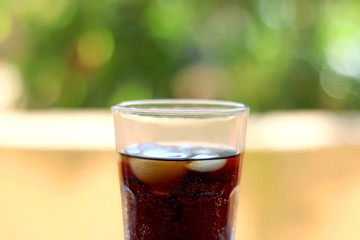 Glass of soda with ice. Selective focus, garden in the background.