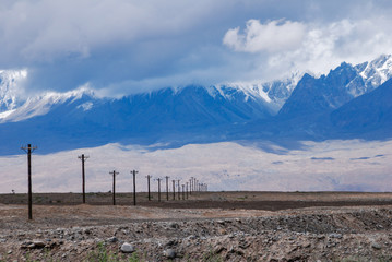 Electric poles crossing the valley in Karakoram . White peaks in clouds in the far background. China.