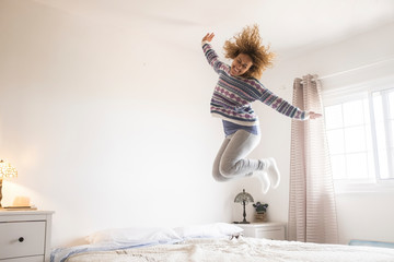 Concept of covid-19 coronavirus lockdown quarantine stay home concept - joyful and happy activity at home with cheerful single adult woman jumping on the bedroom