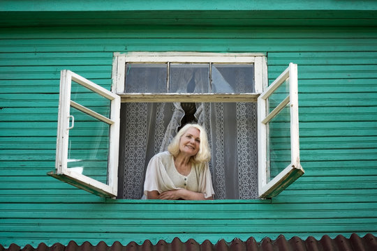 woman grandmother standing near window looking outdoor in green wooden house