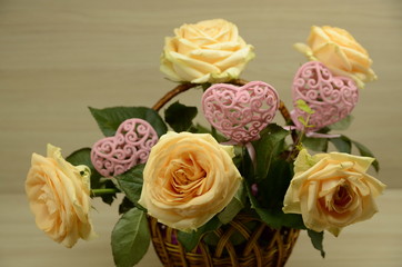On a white background is a basket with fresh pink roses and decorative, openwork hearts.