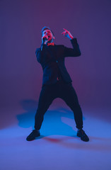Fototapeta na wymiar Young caucasian musician, performer singing on gradient purple-blue background in neon light. Concept of music, hobby, festival. Joyful party host, DJ, stand upper, singer. Colorful portrait of artist