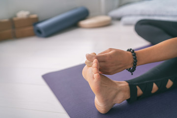 Yoga stretching at home girl stretches big toe pull stretch exercises woman doing hamstring warm up at home on fitness mat training stretching legs wearing mala bracelet.