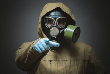 Man in gas mask is showing ahead by his index finger close up on gray background.