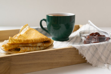 Pancakes (Russian Blini) with strawberry jam and tea on a tray. Breakfast. Сlose up.