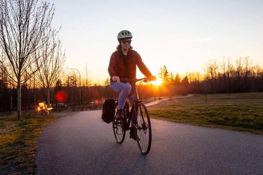Caucasian Woman Riding a Bicycle on a Pedestrian Path during a sunny sunset. Taken in Surrey, Vancouver, British Columbia, Canada.