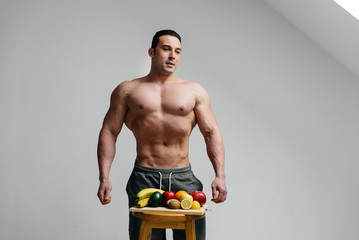 Sexy vegan guy with a naked torso posing in the Studio next to fruit. Diet. Healthy diet