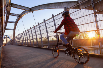 Caucasian Woman Riding a Bicycle on a Pedestrian Bridge over the Highway during a sunny sunset....