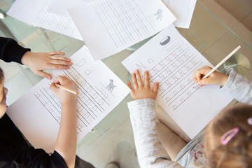 Schoolboy and schoolgirl writing letters. Close-up  pencil in the hand of child. Children learning to write letters at the table. A home distance learning.