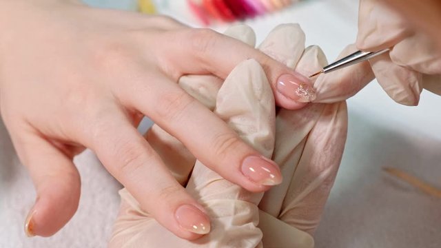 The manicure master applies a shiny nail Polish to the client's nails in a beauty salon. drawing a heart on the client's nails. Close up.