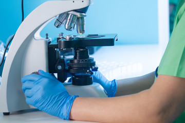 Hands of female in gloves working with light or fluorescent stereo microscope in research...