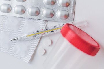 Pills in blisters, a jar for analysis and a thermometer. Treatment and prevention of colds, flu, infections, coronavirus on a white isolated background.