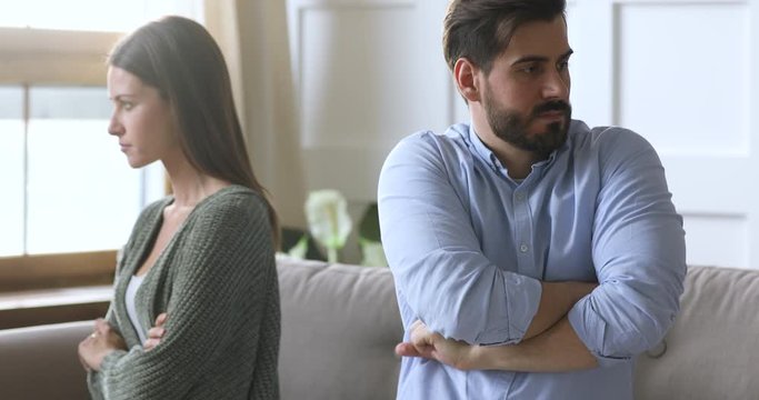 Head shot stressed young couple ignoring each other after quarrel, sitting separately on couch. Unhappy spouses having family psychological problems, suffering from misunderstanding or fight.