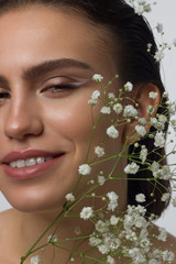 Close up portrait of a face with beautiful skin and nude makeup, eyeliner and long eyelashes, puffy natural lips and white flowers. Fashion photography. Cosmetology and spa. Freshness of spring
