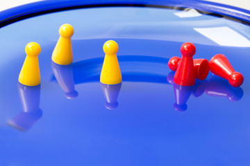 Obraz premium Social distancing concept. Three yellow game pieces keeping distance and three red game pieces grouped, two of them fallen down