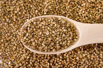 buckwheat in a wooden spoon against the background of buckwheat. Close-up. View from above.