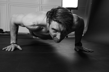 Fototapeta na wymiar Muscular man doing push-ups on one hand against dark background.