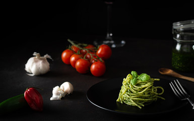 Spaghetti z sosem pesto z zielonym sosem genueńskim ze świeżymi pomidorami na czarnej płycie i czarnym tle z bocznym światłem - 333537774