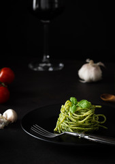 Spaghetti z sosem pesto z zielonym sosem genueńskim ze świeżymi pomidorami na czarnej płycie i czarnym tle z bocznym światłem - 333537786