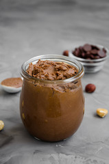 Homemade crispy chocolate hazelnut paste in a glass jar on a dark background. Vertical orientation.