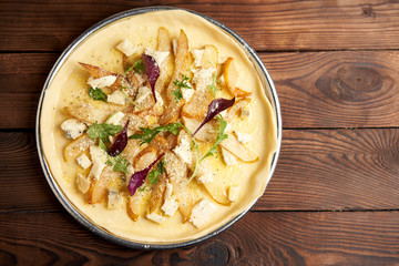 vegetarian raw pizza with gorgonzola cheese and pear on a metal plate ready to cook