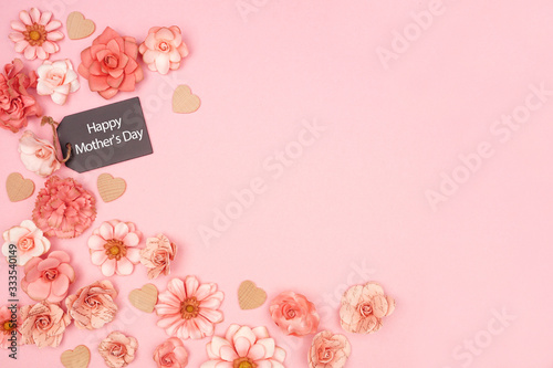 Happy Mothers Day chalkboard gift tag with corner border of pink paper flowers. Above view over a pink background. Copy space.