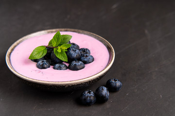 Tasty fresh blueberry yoghurt shake dessert in ceramic bowl standing on black dark table background.