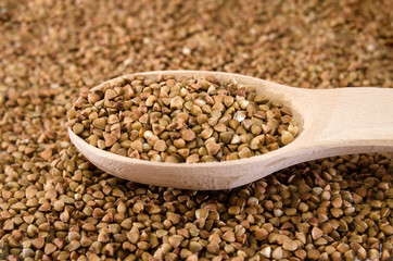 buckwheat in a wooden spoon against the background of buckwheat. Close-up.