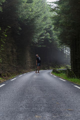 young man in a cap seems to float on a road that runs through a pine forest covered by mist