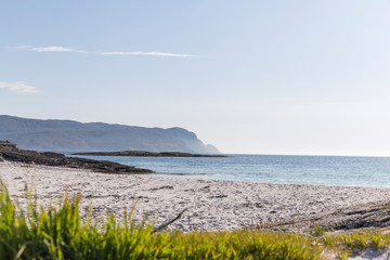 colorful contrasts, white sand beach, and crystal clear blue sea, mountains, green grass, some rocks and clear blue sky
