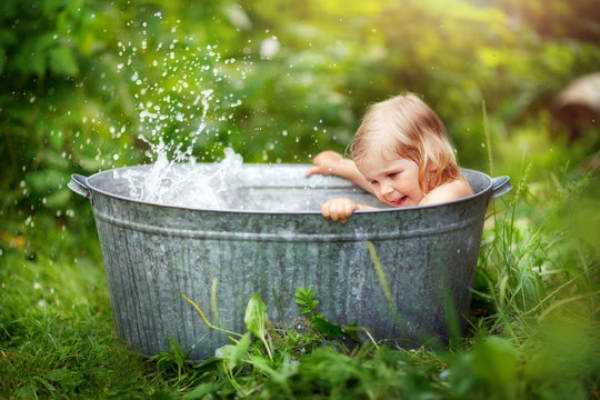 girl bathing in a basin on the street, water splashes, summer in the village, happy childhood, children's laughter